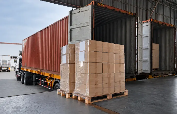 Wrapped cartons on pallets beside shipping containers for export loading